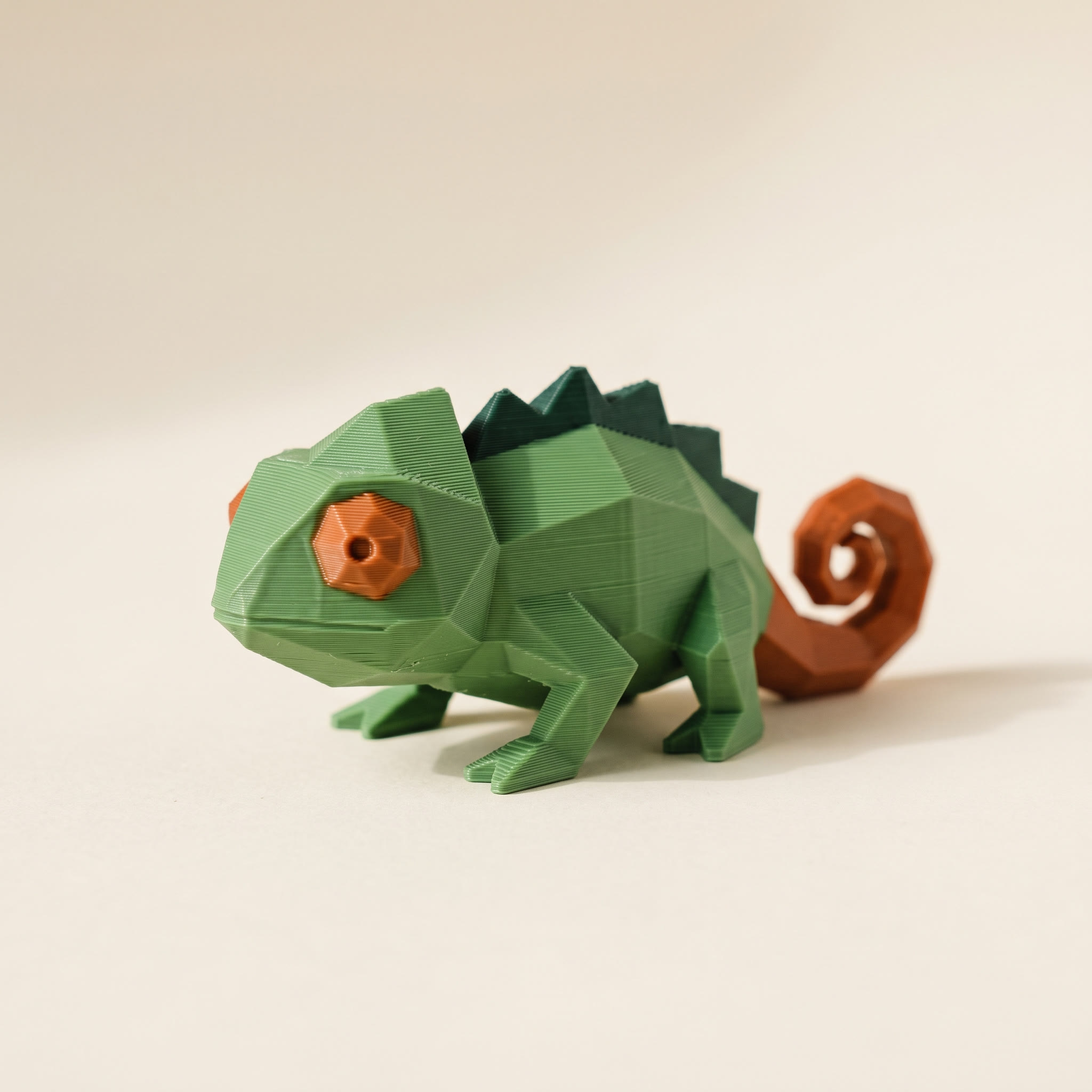 A low-poly multi-color 3D-printed chameleon showing separate green and orange filament regions assigned per surface