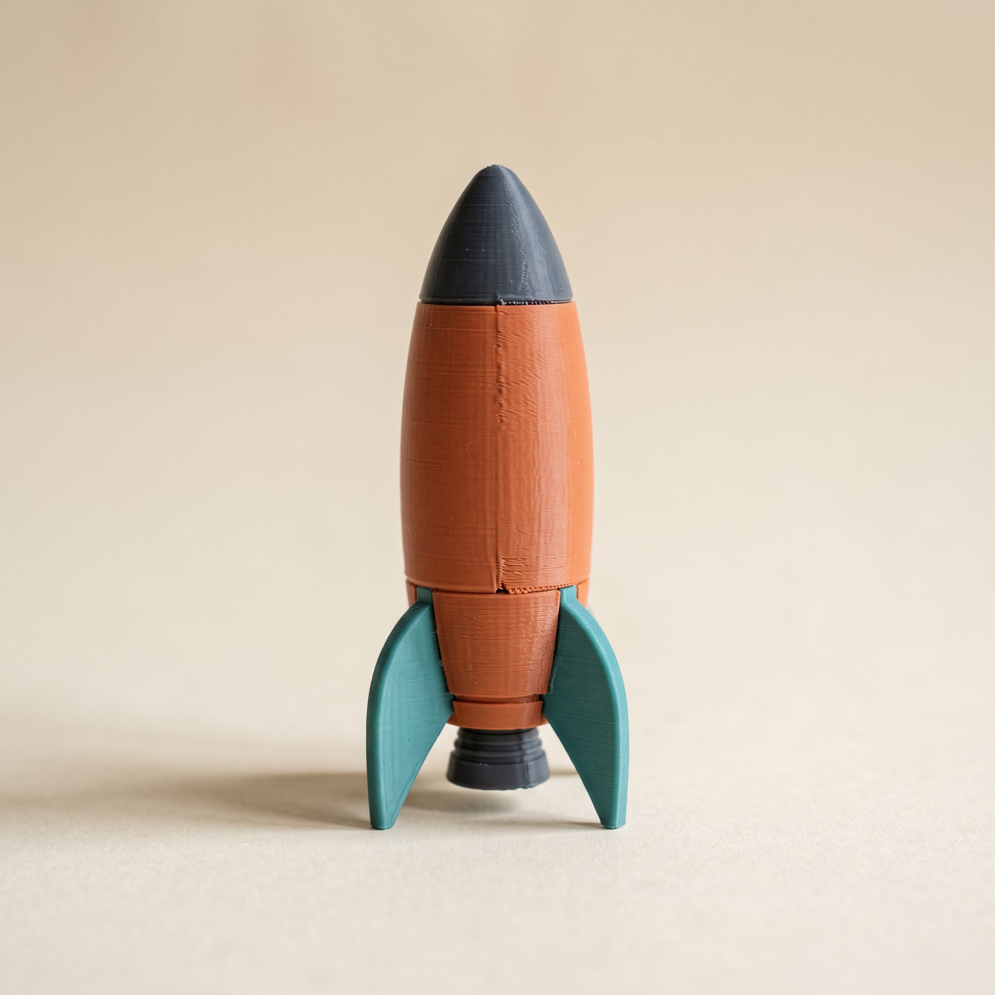 A multi-color FDM 3D-printed retro toy rocket in terracotta, teal, and charcoal filament on a cream background