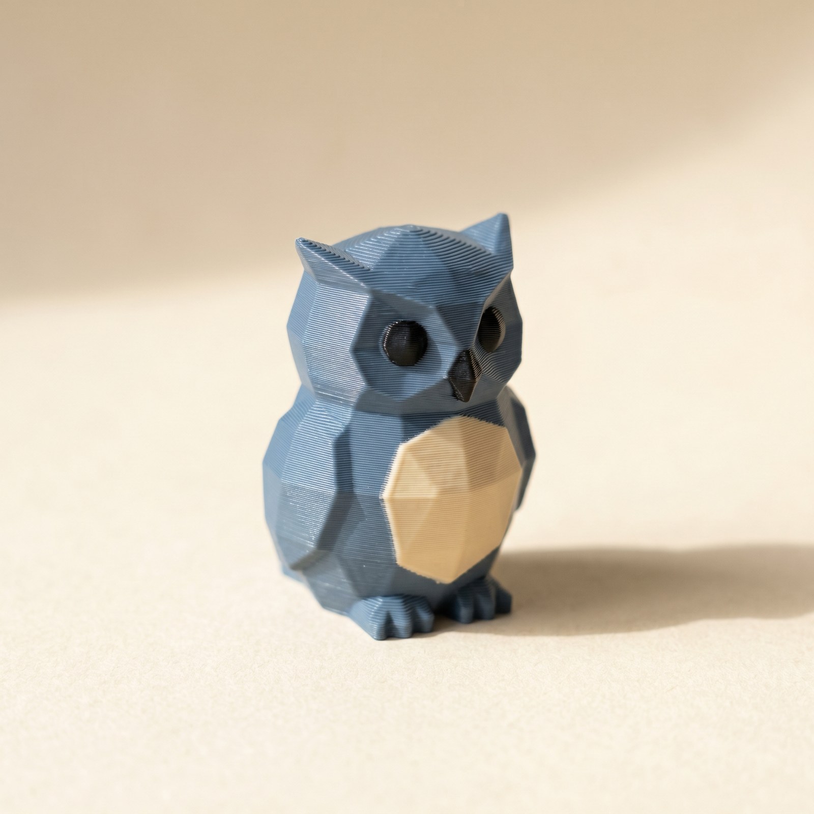 A multi-color 3D printed low-poly owl figurine in slate blue and cream filament, showing how palette ordering affects FDM print results