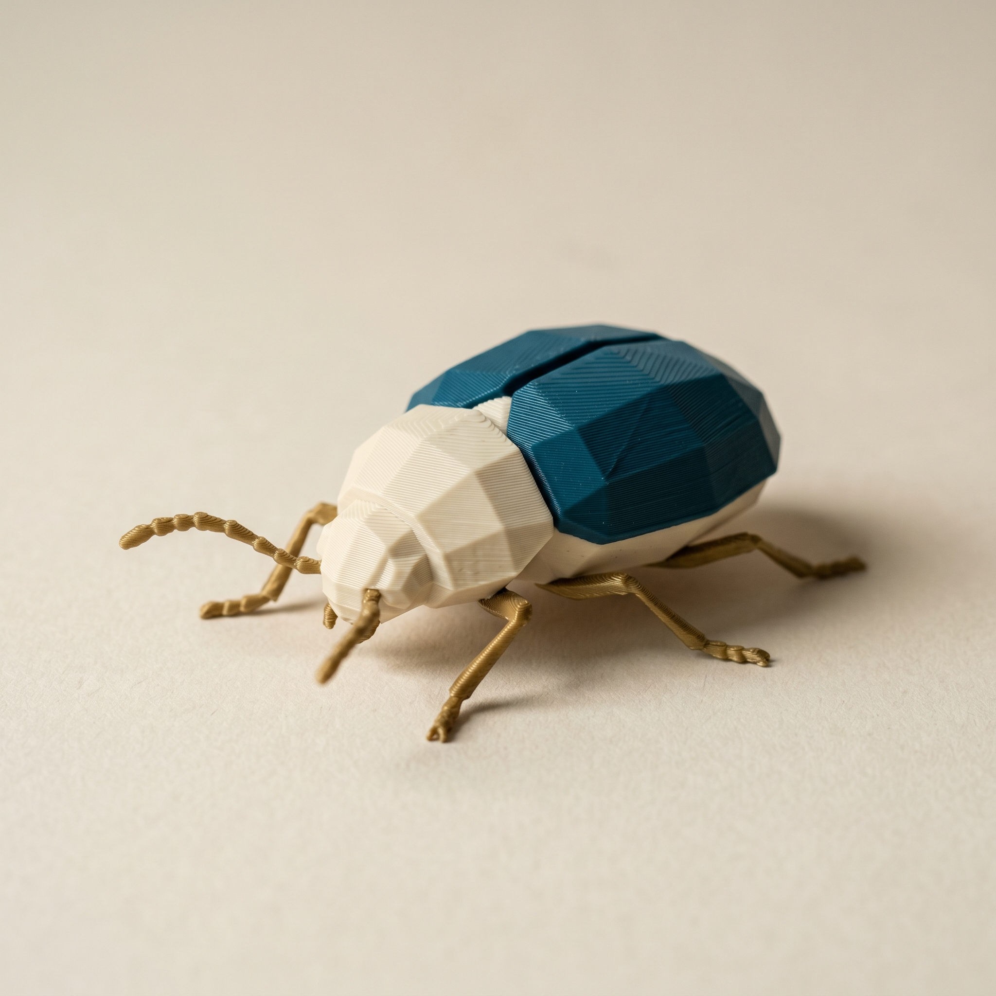 A multi-color FDM 3D-printed low-poly armored beetle figurine with matte cream carapace, deep teal wing covers, and thin brass-gold legs and antennae on cream paper