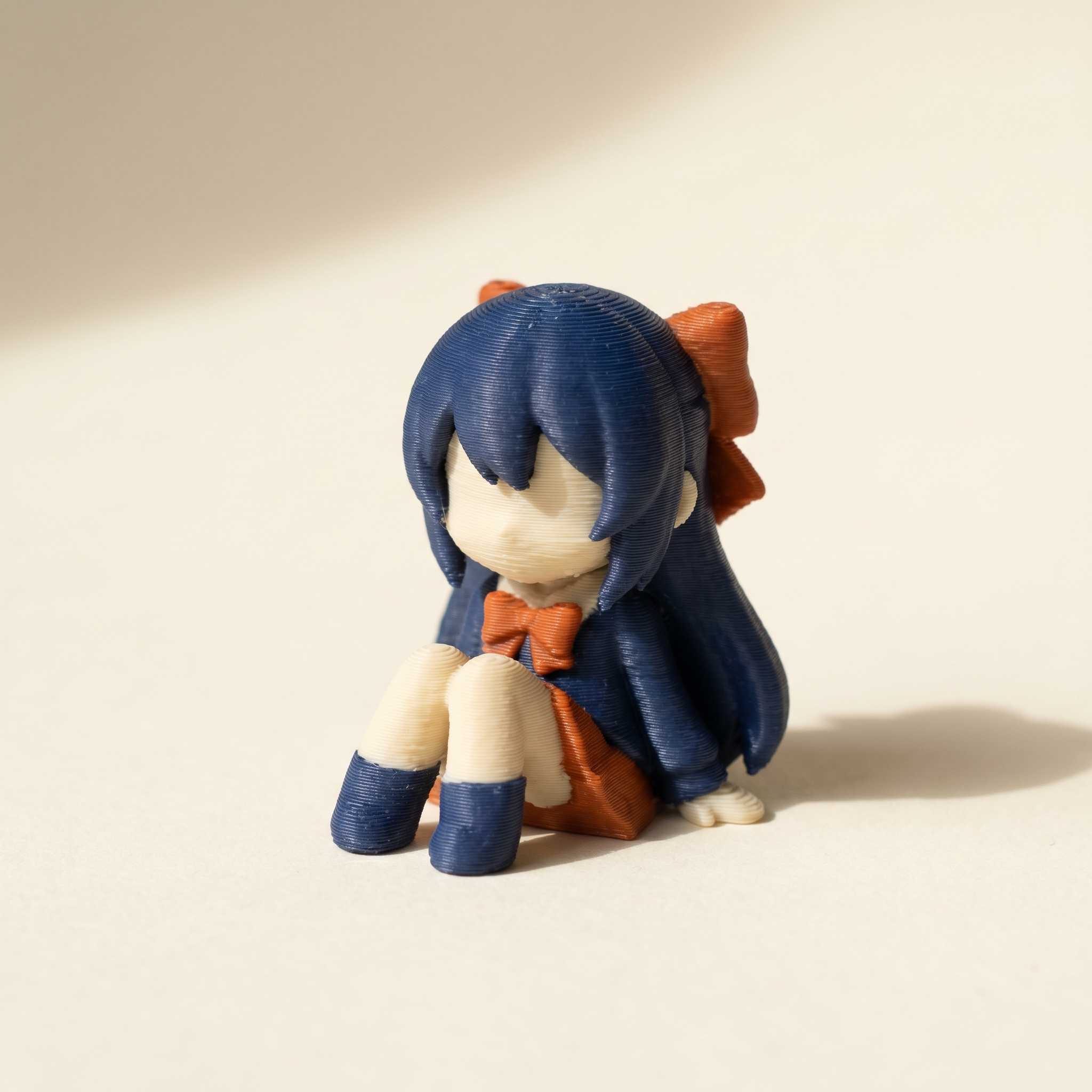 A multi-color FDM 3D-printed anime-style figurine in matte navy blue, cream, and burnt orange filament on cream paper