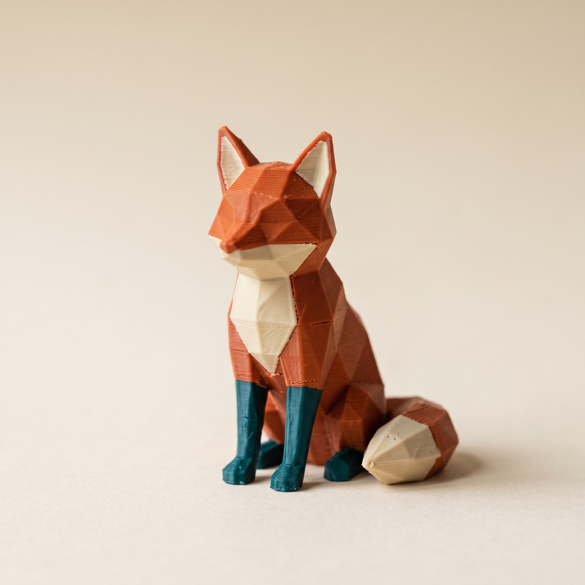 Low-poly fox printed in orange, cream and teal filament, the kind of model people load into an STL editor to resize or recolor