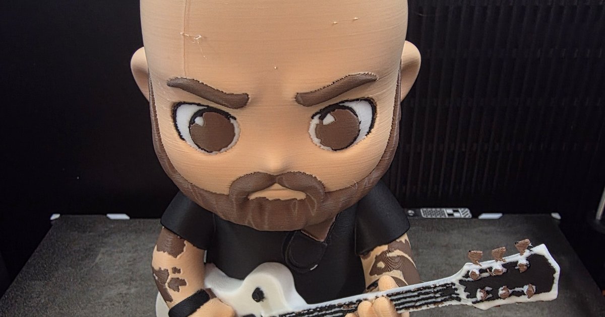 A 3D printed chibi figure of a bearded man holding a white electric guitar, on the printer bed